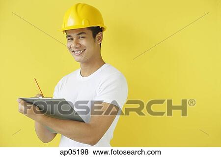 Man wearing hardhat, writing on clipboard, smiling at camera View Large Photo Image Stock Photo - Man wearing hardhat, writing on clipboard, smiling at camera. Fotosearch