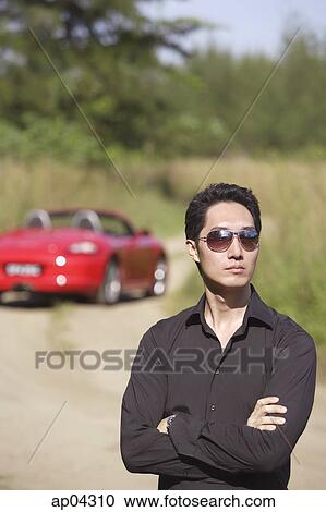 Man wearing sunglasses, arms crossed, red sports car in the background View Large Photo Image Stock Image - Man wearing sunglasses, arms crossed, red sports car in the background. Fotosearch