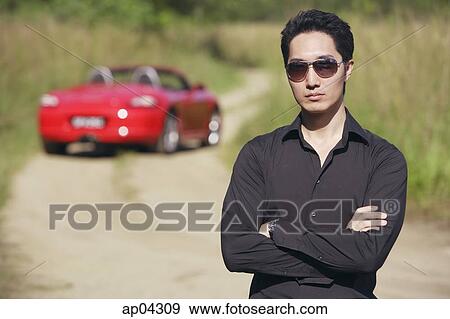 Man wearing sunglasses, arms crossed, facing camera, red sports car in the background View Large Photo Image Stock Photo - Man wearing sunglasses, arms crossed, facing camera, red sports car in the background. Fotosearch