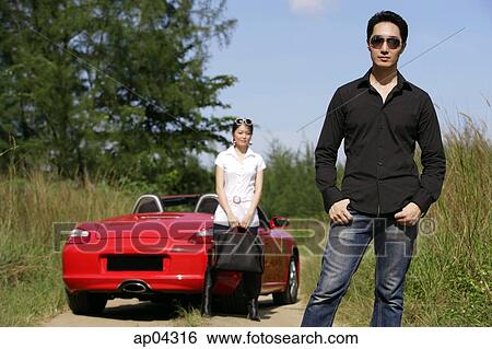 Man wearing sunglasses, facing camera, woman and red sports car in the background View Large Photo Image Stock Photograph - Man wearing sunglasses, facing camera, woman and red sports car in the background. Fotosearch