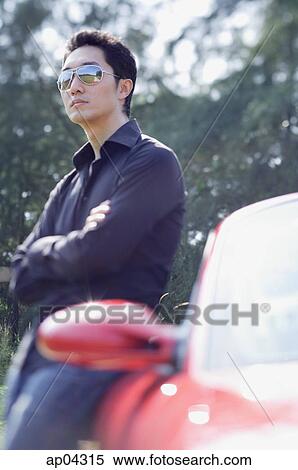 Man wearing sunglasses, leaning on red sports car, looking away View Large Photo Image Stock Photography - Man wearing sunglasses, leaning on red sports car, looking away. Fotosearch