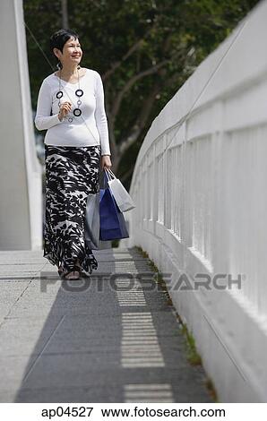 Mature woman carrying shopping bags, walking along bridge View Large Photo Image Stock Photo - Mature woman carrying shopping bags, walking along bridge. Fotosearch