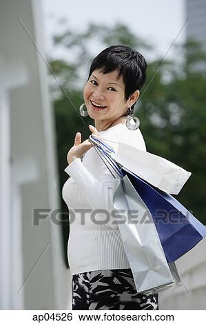 Mature woman carrying shopping bags, looking over shoulder View Large Photo Image Stock Photograph - Mature woman carrying shopping bags, looking over shoulder. Fotosearch