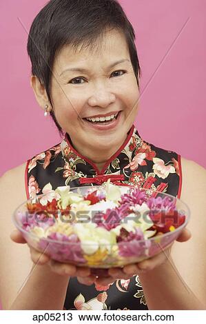 Stock Image - Mature woman holding bowl of flowers, smiling. Fotosearch