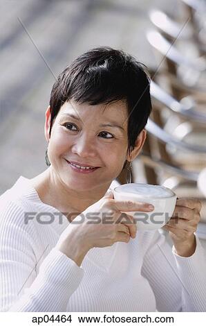 Mature woman holding coffee cup, looking away, smiling View Large Photo Image Picture - Mature woman holding coffee cup, looking away, smiling. Fotosearch