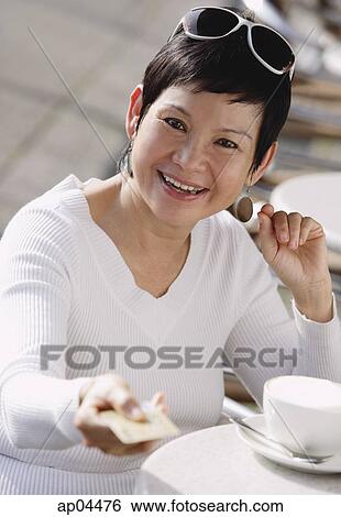 Stock Photograph - Mature woman in cafe holding out credit card. Fotosearch