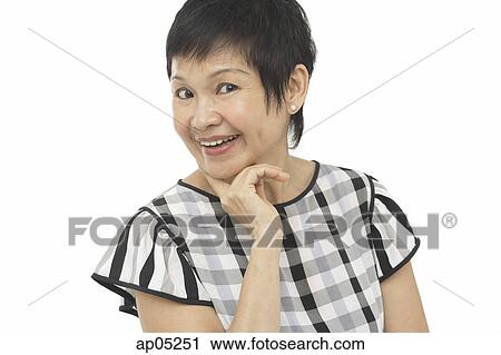 Stock Image - Mature woman in checked top, hand on chin, smiling at camera. Fotosearch