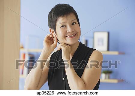 Mature woman putting on earrings View Large Photo Image Stock Photograph - Mature woman putting on earrings. Fotosearch