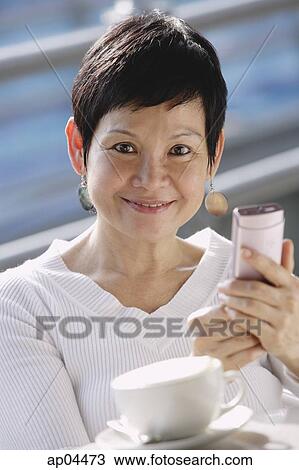 Stock Image - Mature woman with mobile phone, looking at camera. Fotosearch