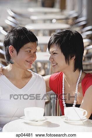 Stock Image - Mother and adult daughter in cafe, smiling at each other. Fotosearch
