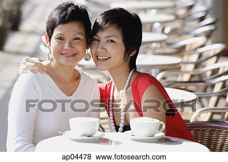 Stock Photo - Mother and adult daughter in cafe, smiling at camera. Fotosearch