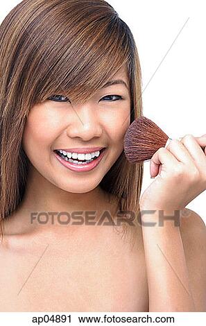 Stock Image - Teenage girl holding make-up brush to face. Fotosearch
