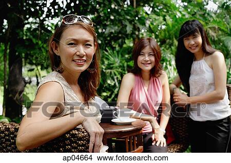 Picture - Three women at outdoor garden cafe, looking at camera, smiling. Fotosearch