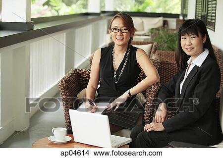 Two businesswomen sitting on patio with laptop, looking at camera View Large Photo Image Picture - Two businesswomen sitting on patio with laptop, looking at camera. Fotosearch