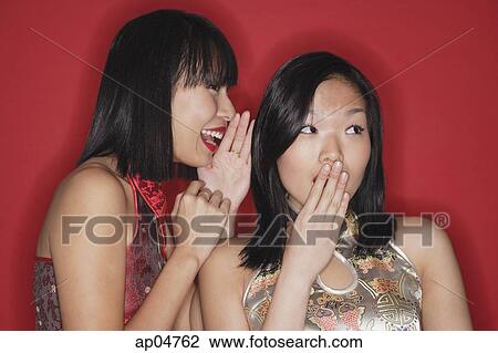 Stock Image - Two women against red background, whispering. Fotosearch