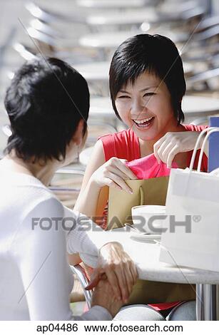 Stock Photograph - Two women at cafe with shopping bags, over the shoulder view. Fotosearch