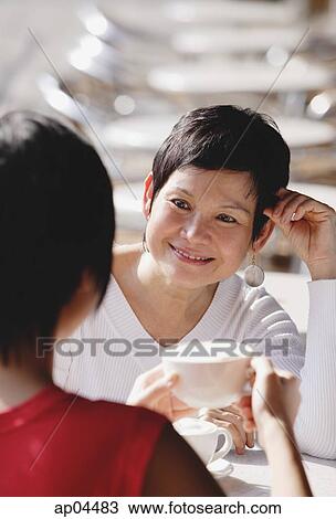 Stock Image - Two women having coffee, over the shoulder view. Fotosearch