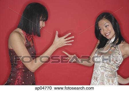 Stock Image - Two women in cheongsams, playing hand game. Fotosearch