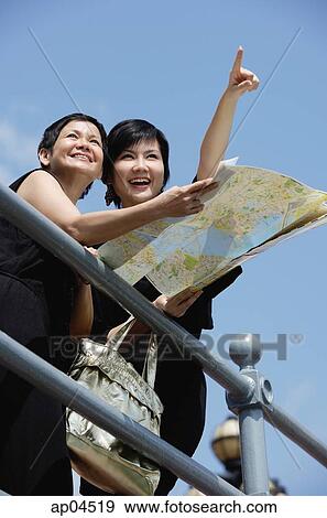 Two women side by side, one pointing in the distance, the other holding map View Large Photo Image Stock Photo - Two women side by side, one pointing in the distance, the other holding map. Fotosearch