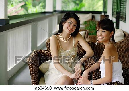 Two young women sitting on patio, smiling at camera View Large Photo Image Stock Image - Two young women sitting on patio, smiling at camera. Fotosearch