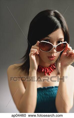 Stock Image - Woman adjusting large sunglasses, looking at camera. Fotosearch