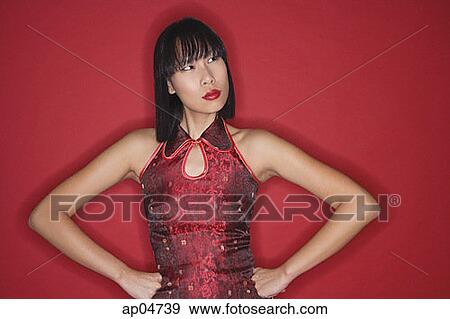 Stock Photo - Woman against red background, dressed in cheongsam, hands on hips. Fotosearch