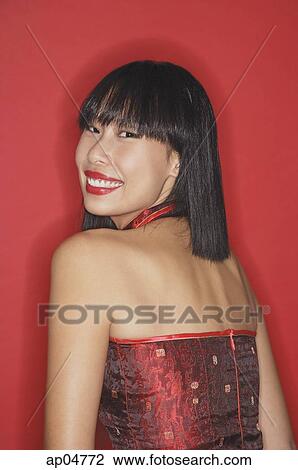 Stock Image - Woman against red background, looking over shoulder, smiling. Fotosearch
