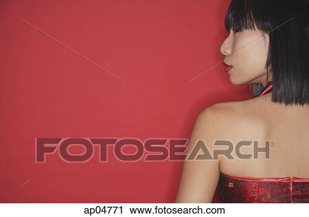 Stock Image - Woman against red background, rear view. Fotosearch