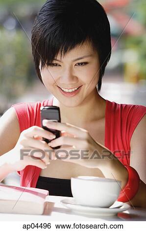 Stock Photograph - Woman at cafe using mobile phone, text messaging. Fotosearch
