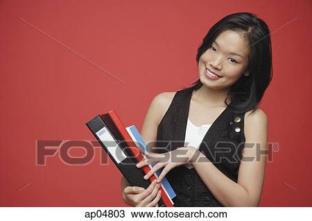 Stock Image - Woman carrying books, looking at camera, smiling. Fotosearch