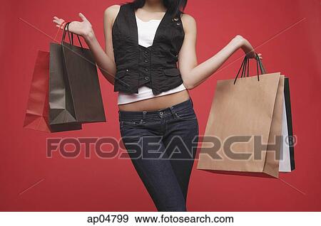 Stock Photo - Woman carrying shopping bags, mid-section. Fotosearch
