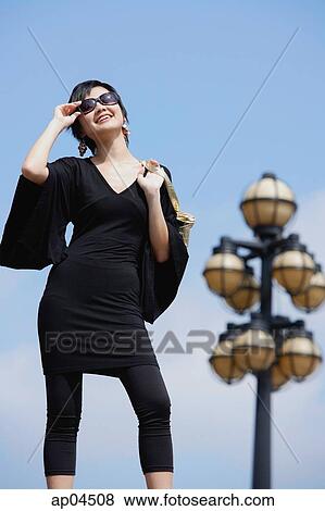 Woman dressed in black, carrying bag over shoulder, adjusting sunglasses View Large Photo Image Stock Photo - Woman dressed in black, carrying bag over shoulder, adjusting sunglasses. Fotosearch