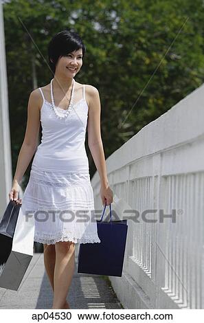Stock Image - Woman dressed in white carrying shopping bags. Fotosearch