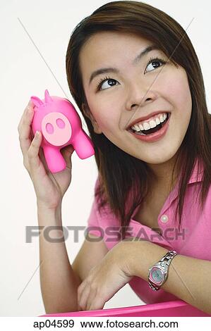 Stock Photo - Woman holding pink piggy bank to ear. Fotosearch