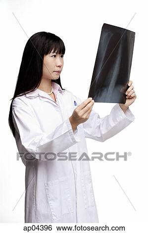 Woman in lab coat, looking at X-ray View Large Photo Image Stock Photograph - Woman in lab coat, looking at X-ray. Fotosearch