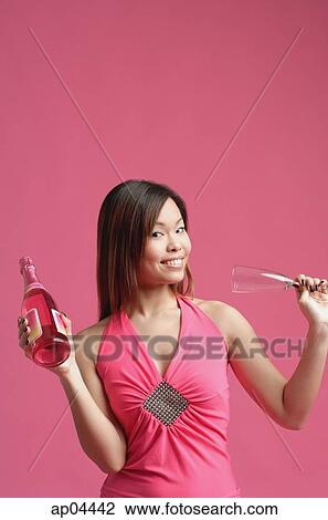 Stock Image - Woman in pink dress, holding champagne bottle and champagne glass. Fotosearch