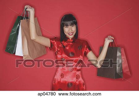 Stock Image - Woman in red cheongsam, carrying shopping bags, smiling at camera. Fotosearch