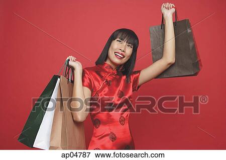 Stock Photo - Woman in red cheongsam, carrying shopping bags, looking up. Fotosearch