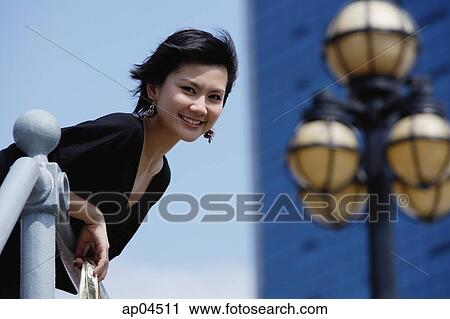 Stock Image - Woman leaning over railing, smiling at camera. Fotosearch