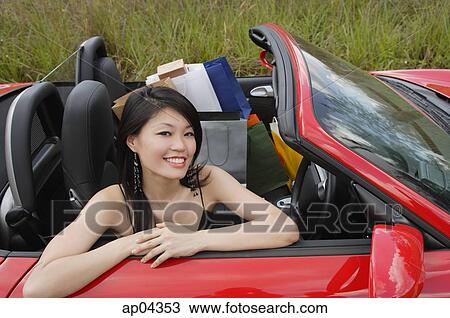 Stock Image - Woman sitting in convertible car, shopping bags next to her, smiling at camera. Fotosearch