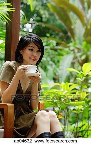 Stock Image - Woman sitting on patio, holding cup and saucer. Fotosearch