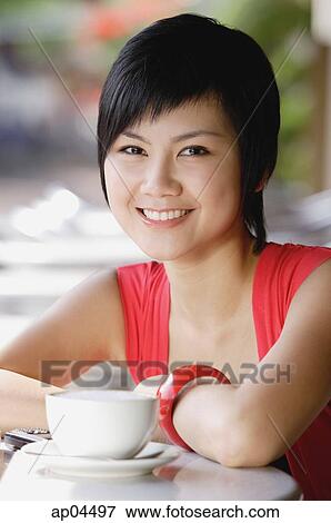 Stock Photo - Woman smiling at camera, cup and saucer next to her. Fotosearch