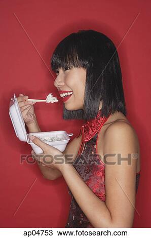 Stock Image - Woman standing red background, eating rice from a Styrofoam container. Fotosearch