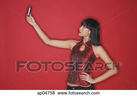 Stock Photo - Woman using mobile phone to take a picture of herself, hand on hip. Fotosearch