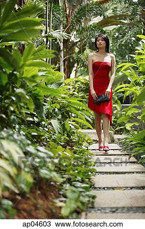 Woman walking along garden path, wearing red dress View Large Photo Image Stock Image - Woman walking along garden path, wearing red dress. Fotosearch