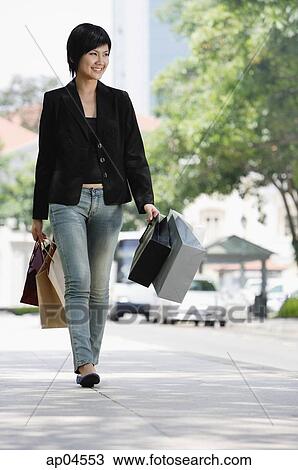 Stock Image - Woman walking in city, holding shopping bags. Fotosearch
