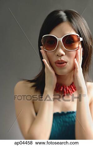 Stock Photo - Woman wearing large sunglasses, hands on face. Fotosearch