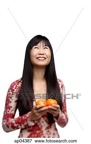 Stock Photo - Woman with long straight hair, holding two oranges, looking up. Fotosearch