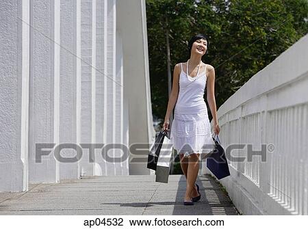 Stock Image - Woman with shopping bags, walking along bridge. Fotosearch