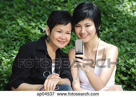 Women side by side, smiling, looking at mobile phone View Large Photo Image Stock Photo - Women side by side, smiling, looking at mobile phone. Fotosearch